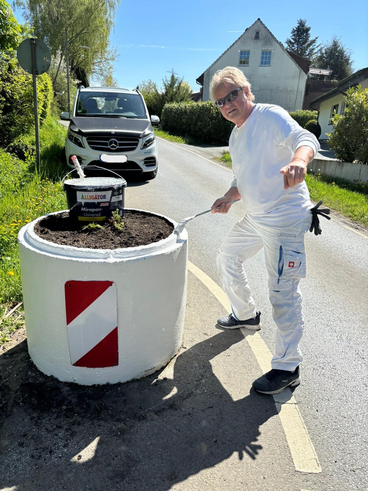 Mitarbeiter von Alligator streicht Straßenpoller in der Farbe Weiß.
